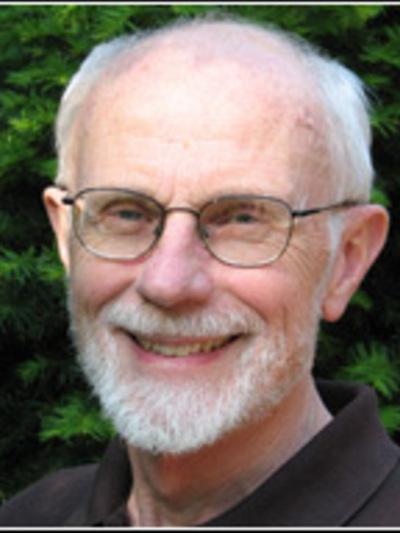 A headshot of a person with a beard and metal frame glasses outdoor, smiling.