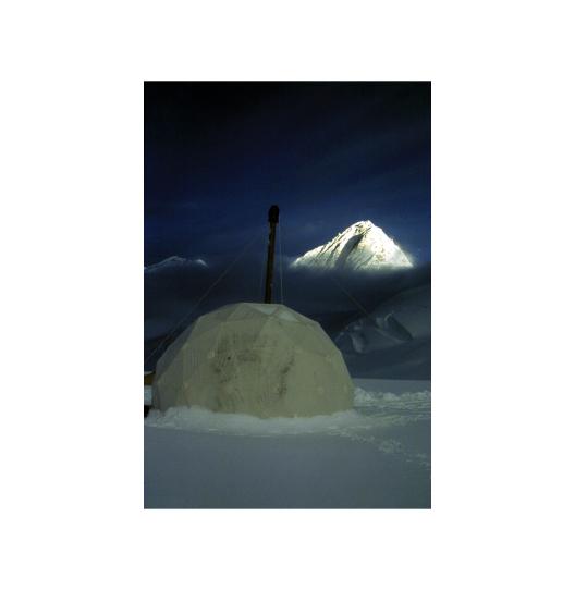 A white domed drill site in snow and a white snow capped mountain at a distance 