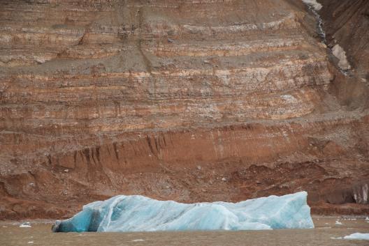 The remnants of ice in the foreground against a wall ofreddish dirt mountain.