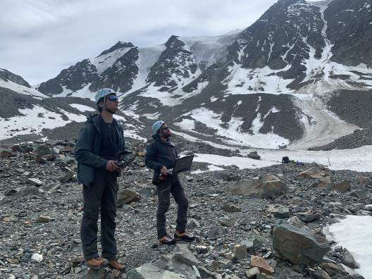 Two people in a snow covered, rocky field working with equipment.