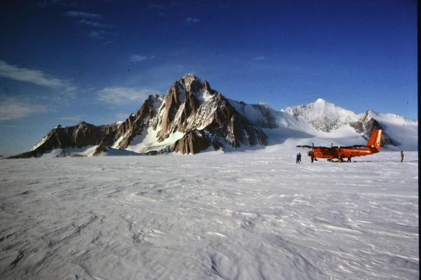 Snowy fiend with a mountain and a red small twin plane under blue skies
