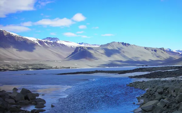 Snow and water in a rocky landscape. Mountains are in the background against a bright blue sky