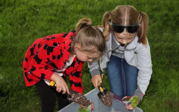 Two children standing over a container carefully shoveling dirt into plant containters