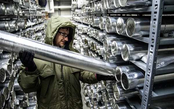 Man holding an ice core in a storage room lined with shelves of ice core 