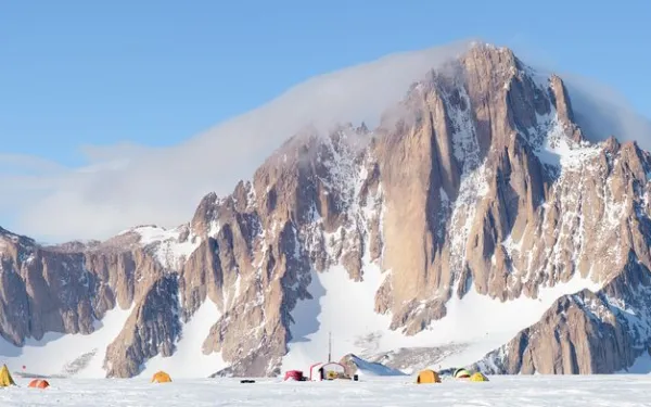 Rocky mountain with some white clouds and blue skies in the background and tents pitched in the foreground.