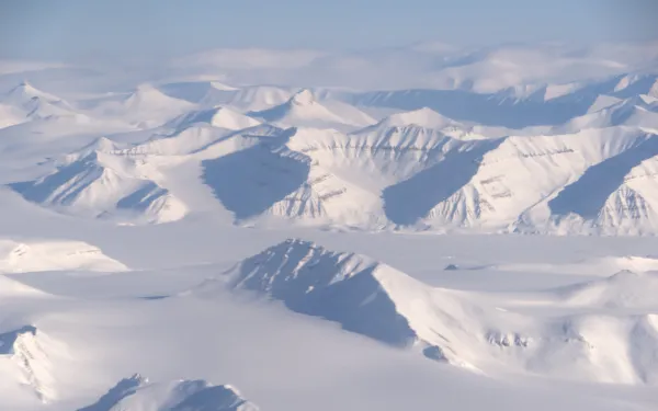 A  series of snow covered mountain ranges at different angles under blue sky.