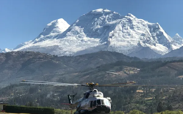 A helicopter parked on a tarmac with a mountain in the background under a clear blue sky.