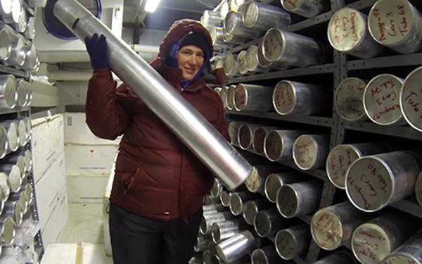 A scientist holding an ice core cyllander inside the ice core storage freezer. There are dozens of cyllanders stored on the shelves.