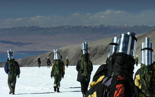A group of people carrying ice core cannisters in backpacks down a snowy mountain