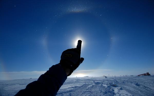 An arm surrounded by ice and pointing at the sky. The pointed finger covers the sun.