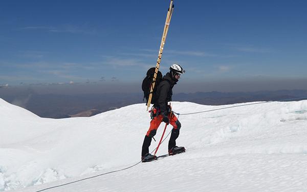 An indvidual wearing sold weather gear, a helmet, and research supplies hikes up a mountain in the arctic 