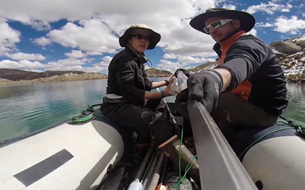 Two researchers are on a small raft on a large body of water. They are wearing hats, sunglasses and other appropriate research gear  