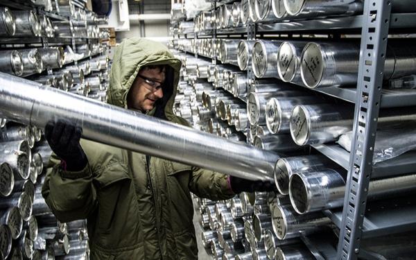 Man holding an ice core in a storage room lined with shelves of ice core 