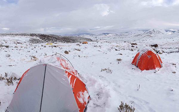 Red and gray tents in snowy research site. The landscape is snowy and rocky with gray skies.