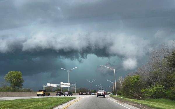 Freeway with cars in different lanes, surrounded by vegetation on the side of the road with blue gray skies and clouds.