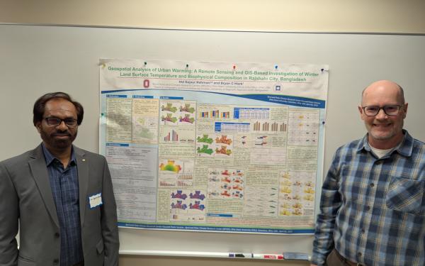 Two people posing with a poster in the middle.