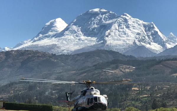 A helicopter parked on a tarmac with a mountain in the background under a clear blue sky.
