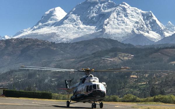 A helicopter parked on a tarmac with a mountain in the background under a clear blue sky.