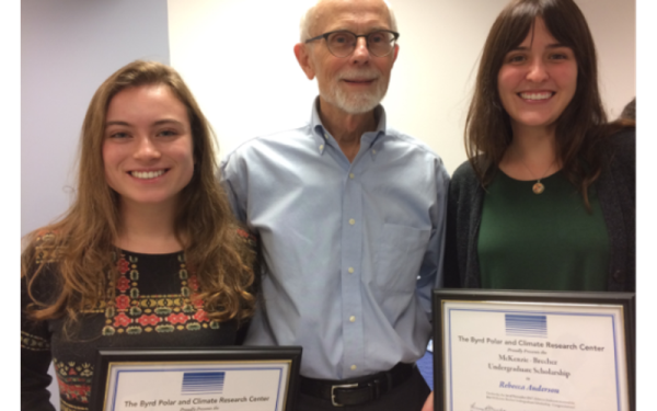 Two people holding certificates on either side of a third person in the middle.