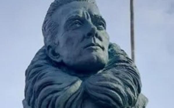 A metal statue on a pedestal with a plaque.