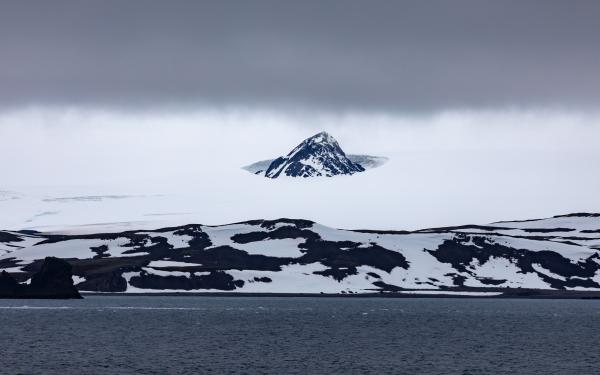 A cold landscape snow covered and an Ocean in the foreground.