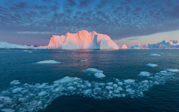sunlit iceberg with scattered sea ice under a pastel arctic sky