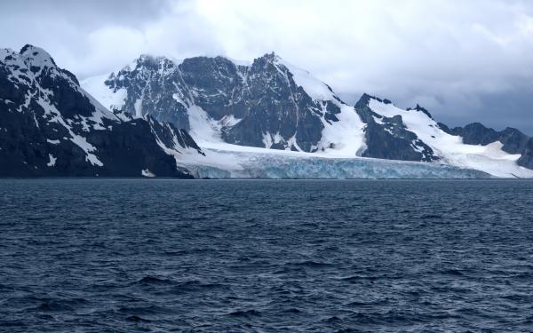 Snow-covered mountains and glacier going into the sea under a cloudy sky.