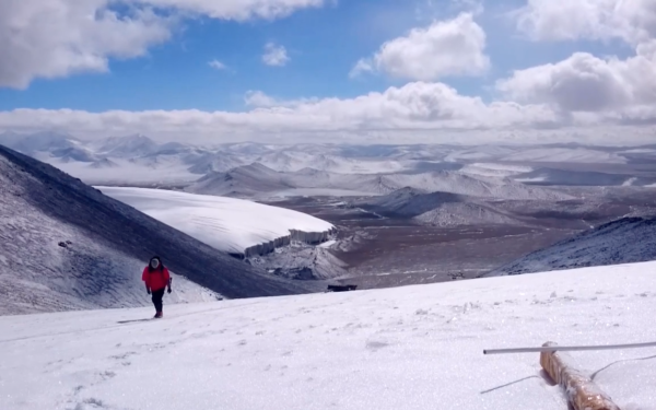 Man walking up glacier with valley and mountains
