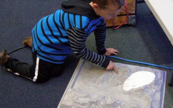 Flubber Glacier Flow Lesson. A young boy plays with a glacier model while sitting on the floor 