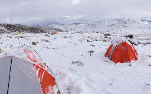 Survival Team Building Lesson. Two orange tents sit covered in snow on a snowy rocky landscape 