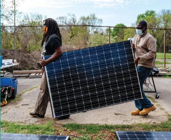 Two men wearing masks carrying a large solar panel outdoors