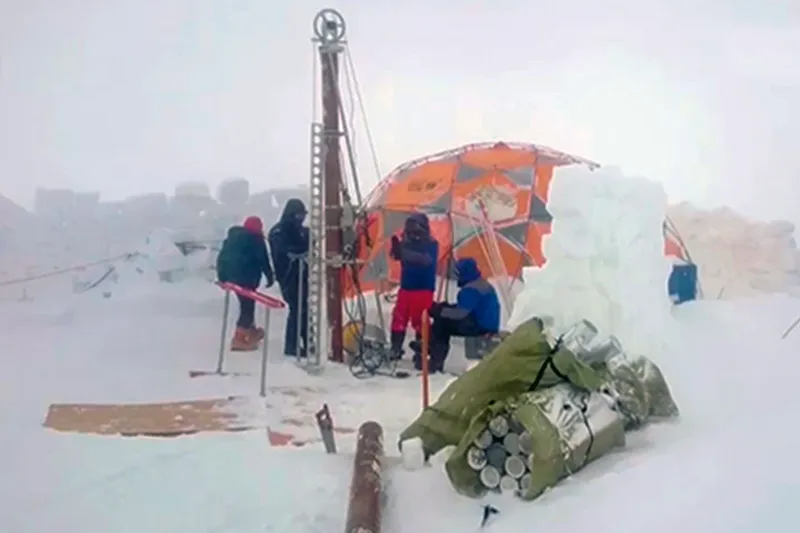 Surrounded by snow, four scientists drill ice cores from the glacier using a tall machine that towers over them