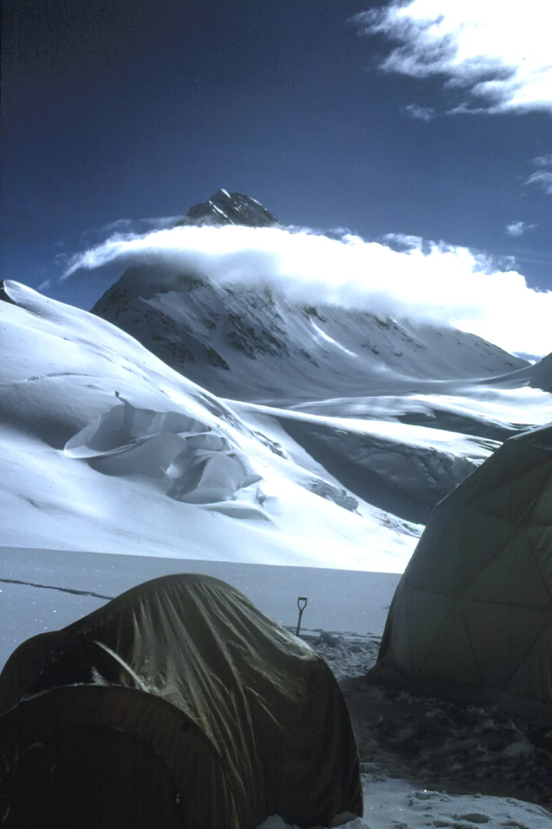 Tents with a background of white mountains and clouds under blue skies.