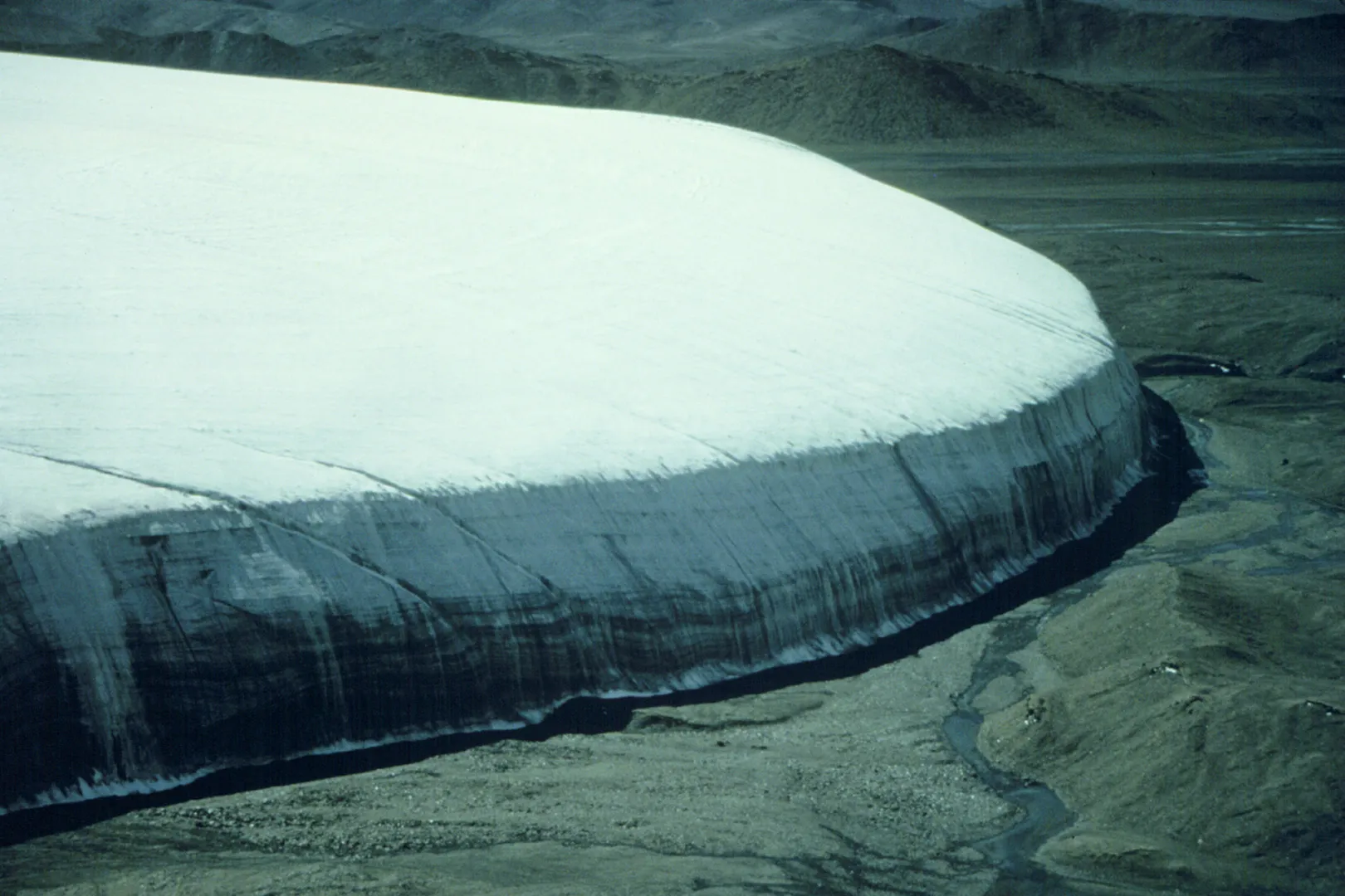 A landscape view of a massive ice cap on a dirt plateau.