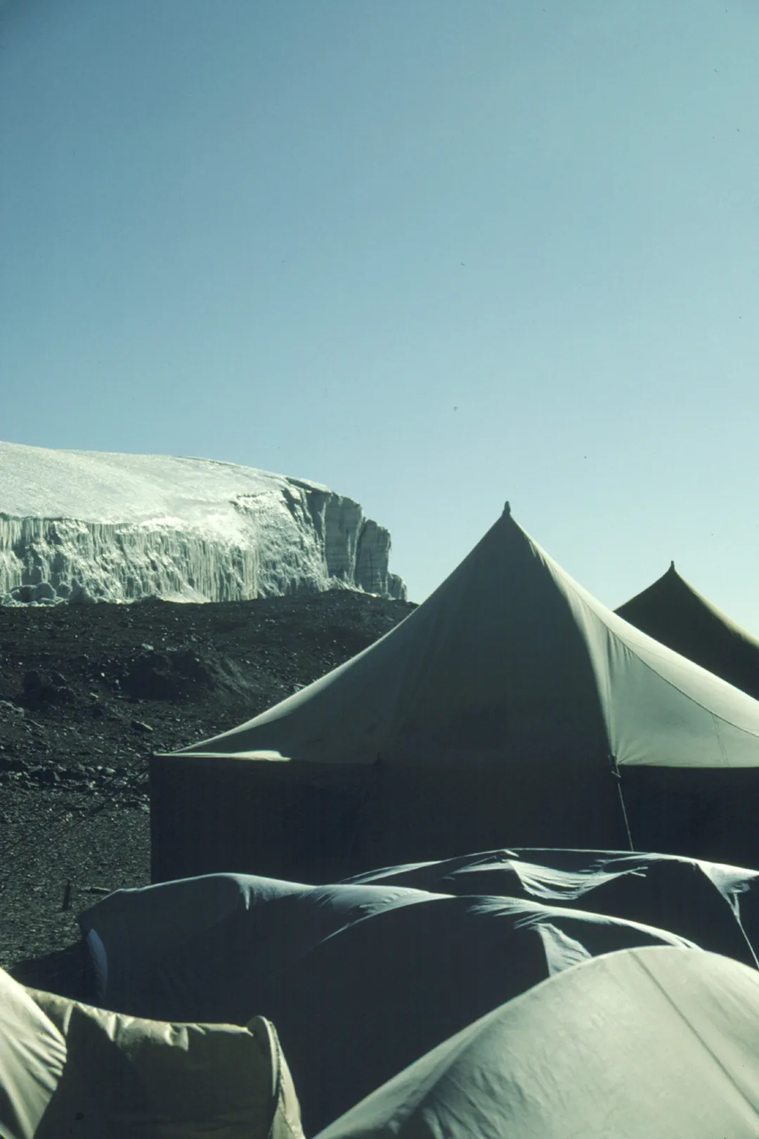 A tent on dirt ground under blue skies with the back drop of the ice cap.