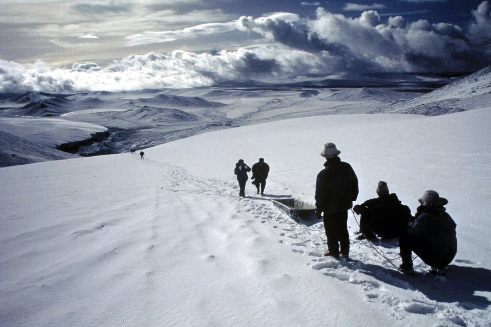 people walking on a snow covered path with a sled under cloudy gray skies. 