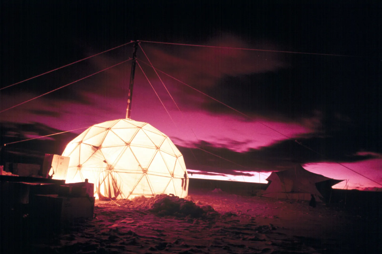 Dome tent lit up in the dark against the pinkish skies.