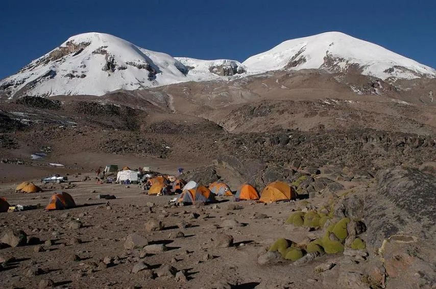 Research site in Coropuna, Peru. The site has tents set up on a rocky landscape. There are snowy mountains in the distance 
