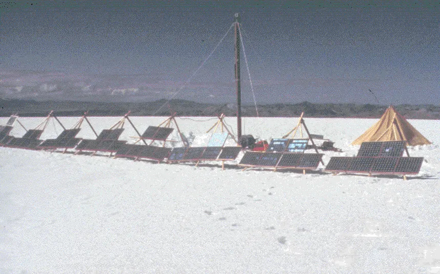 Ice core drill surrounded by solar panels on a snowy landscape.