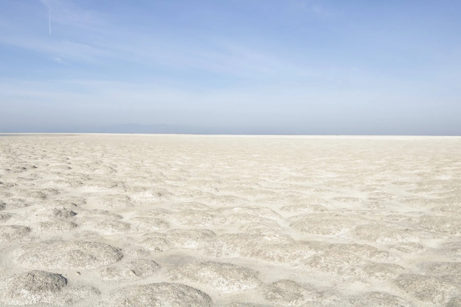 A white field under blue skies with little feather white clouds. 