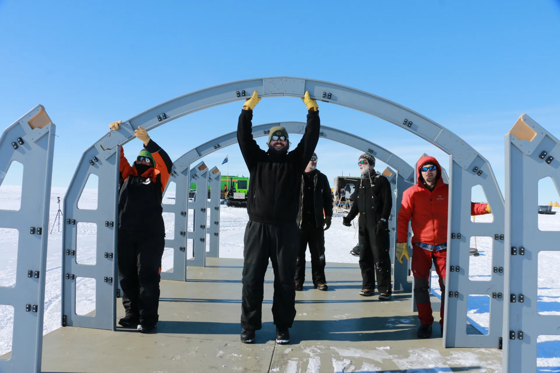 Men erecting the frame for shelter on a concrete slab in a snow flied.