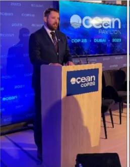 Geoffrey Dipre speaking indoors at a podium. 