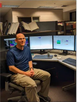 Nathan Patrick sitting at a work station with monitors, keyboards and mouse on the desk .