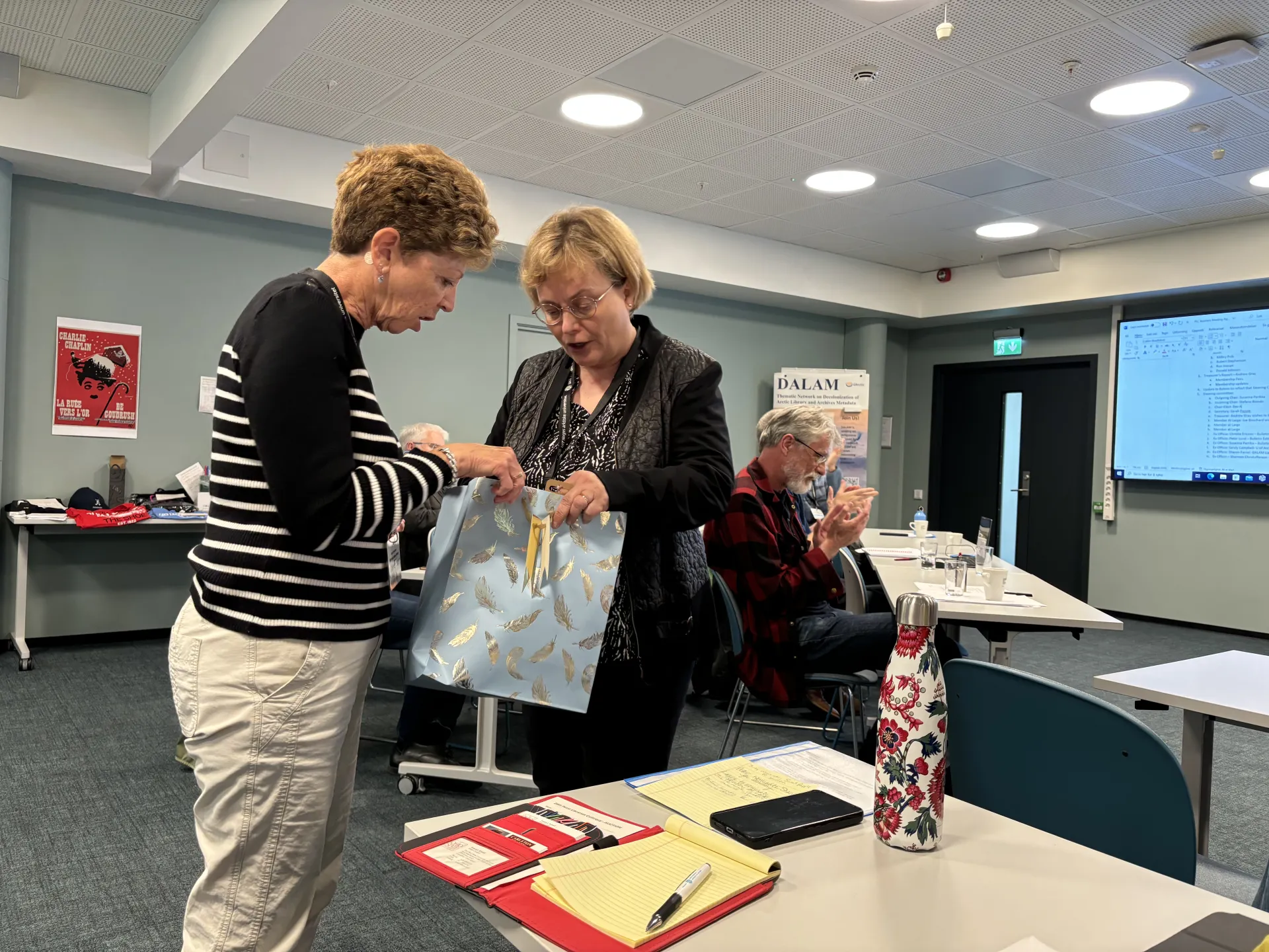 Laura Kissel being presented a gift by a person  in a room with people seated, clapping..