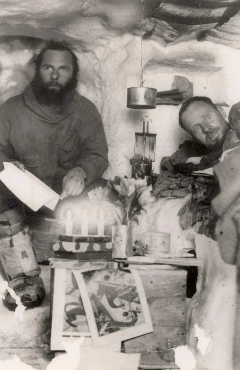 Black and white pic of two men in an igloo with their supplies.