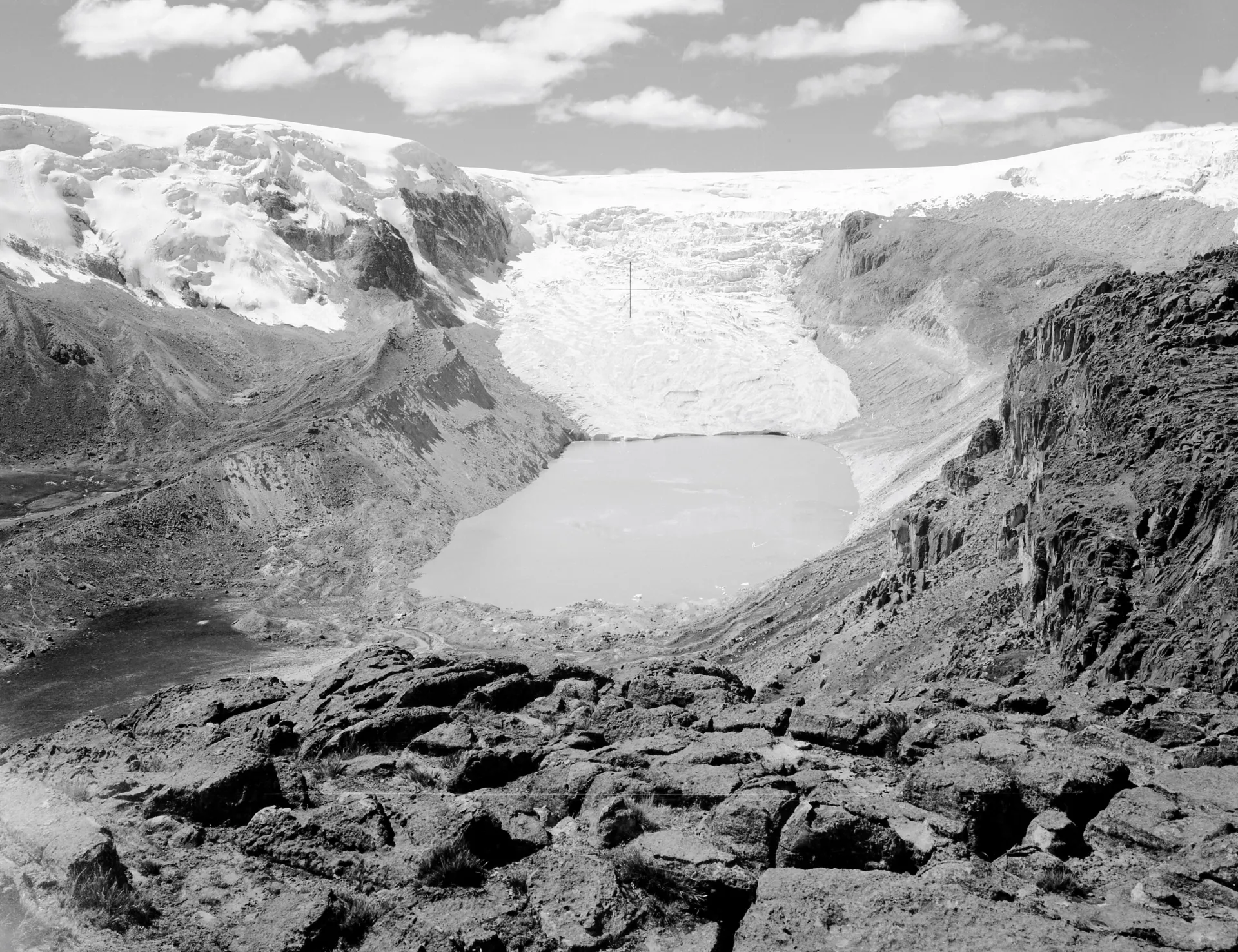 A black and white image of a glacier with a lake in a rocky terrain.