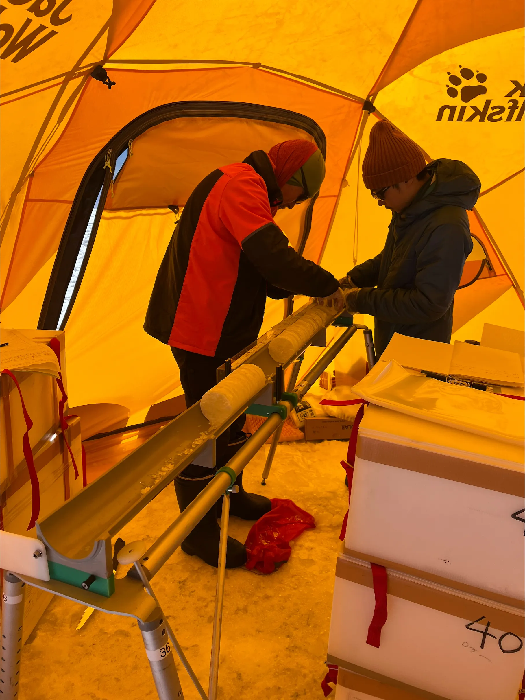 Inside a tent, two people section an ice core on a cradle.