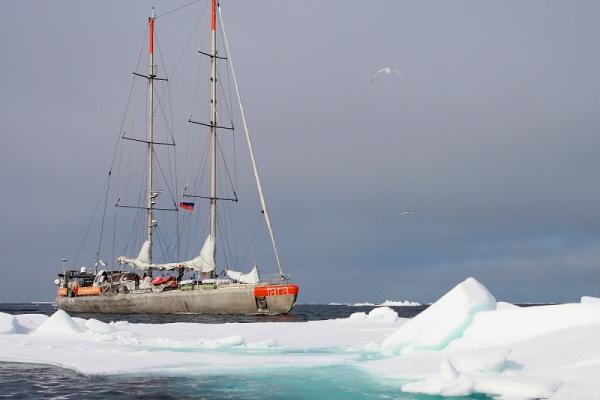 A sailboat sails past a large iceberg