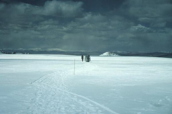 People walking in a distance in a snow covered field under gray, cloudy skies.