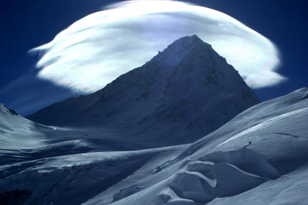 A snowy mountain is backed by cloudy sky.